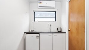 A compact kitchen with a built-in dishwasher, a window above the sink, and a wooden door. - Auckland Akl Airport Motel (Auckland)