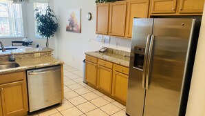 Una cocina con gabinetes de madera, refrigerador de acero inoxidable, lavavajillas y encimera de granito.