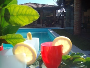A poolside setting with a clear view of a swimming pool, a brick building in the background, and a table with glasses and lemon slices.