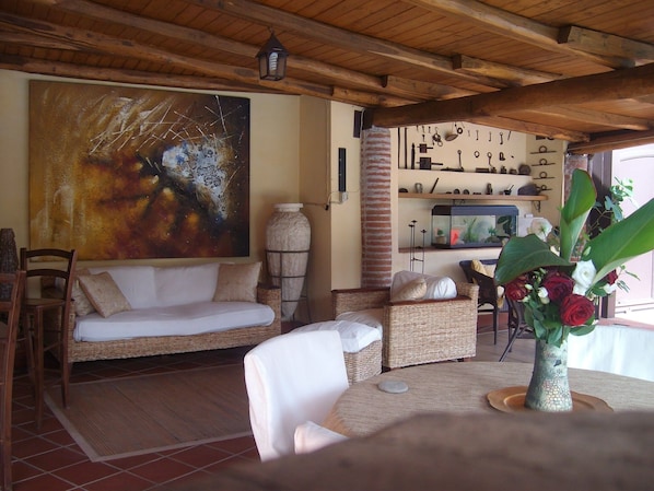 A cozy living area with a sofa, wicker chairs, a table with a vase of flowers, and a large abstract painting on the wall.