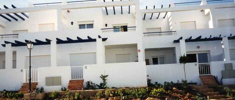 A modern multi-story residential building with balconies, a stone retaining wall, and a well-maintained garden.