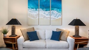 Een woonkamer met een lichtkleurige bank, twee bijzettafels met lampen, en een groot abstract schilderij erboven.