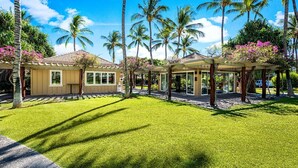 Een resort met een overdekt buitengebied, palmbomen en een verzorgd gazon.