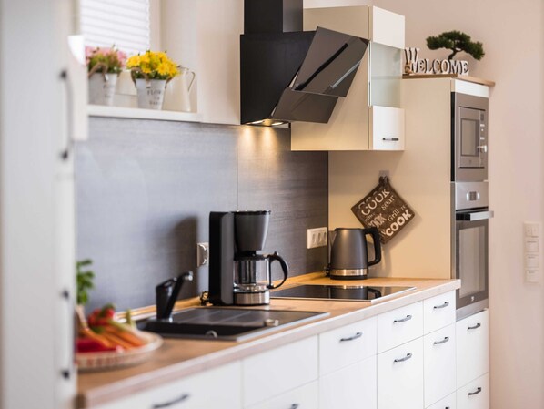 Ett modernt kök med vita skåp, en kaffebryggare, en vattenkokare och en skylt med texten ”Välkommen”.