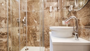A modern bathroom with a glass-enclosed shower, a white sink, and a marble-tiled wall. - Lux Studio (Belgrade)