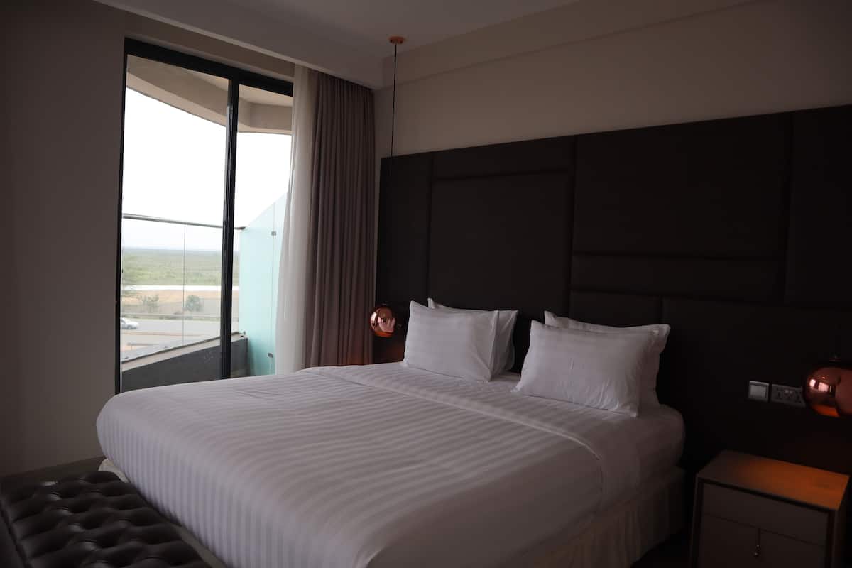 Habitación de hotel con una cama grande, una mesita de noche, una lámpara y una ventana con vistas al paisaje.