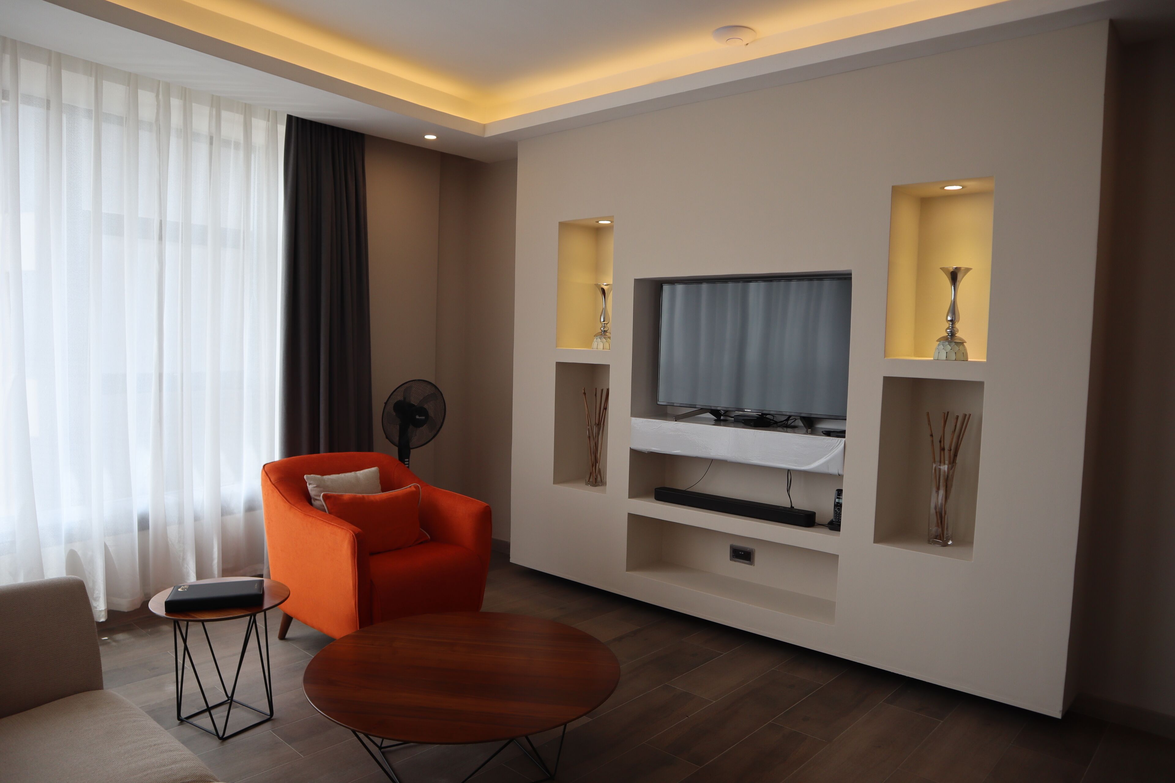 A modern living room with a flat-screen TV, orange armchair, and a small round table.