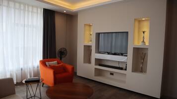 A modern living room with a flat-screen TV, orange armchair, and a small round table.
