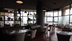 Ein modernes Restaurant mit Holztischen und -stühlen, einer Bar und großen Fenstern mit Blick auf die Stadt.