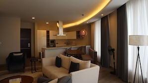 Ein modernes Wohnzimmer mit einer Couch, Couchtisch und einem Essbereich mit Tisch und Stühlen. Es gibt eine Küchenzeile mit Schränken und einer Mikrowelle.