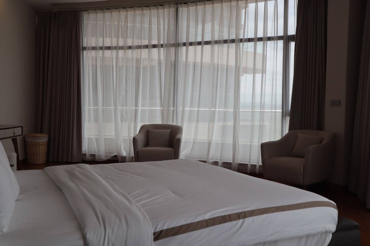 Una habitación de hotel con una cama grande, dos sillones y cortinas de gasa.