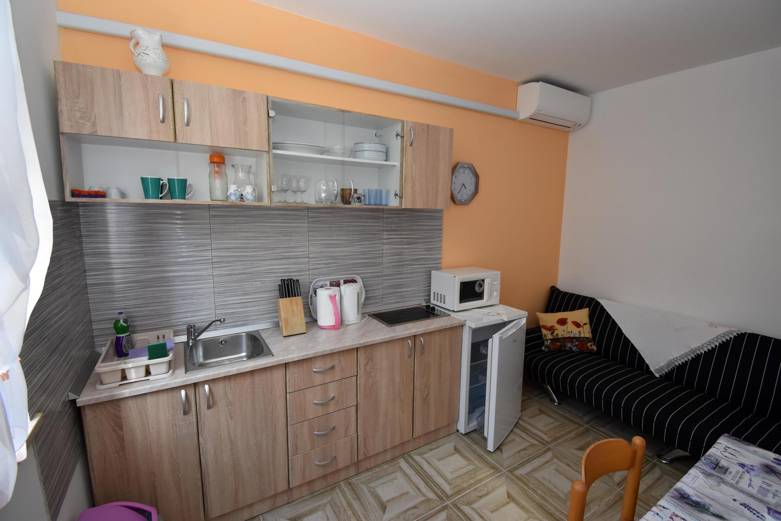Cocina compacta con armarios de madera, microondas y pileta. Incluye un refrigerador pequeño y un comedor con una silla.