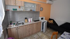 Une cuisine compacte avec des meubles en bois, un four à micro-ondes et un évier. On y trouve également un petit réfrigérateur et un coin repas avec une chaise.