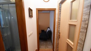 Un couloir étroit avec une douche en verre, une porte en bois et une chambre à coucher visible à travers une porte ouverte.