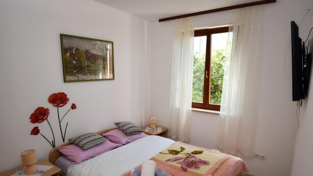 Une chambre à coucher avec un lit, une table de chevet, une lampe, un tableau et une fenêtre avec des rideaux.
