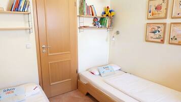 A small, tidy room with two single beds, a wooden door, and shelves with books and toys.