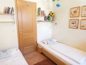 Een kleine, net kamer met twee eenpersoonsbedden, een houten deur en planken met boeken en speelgoed.