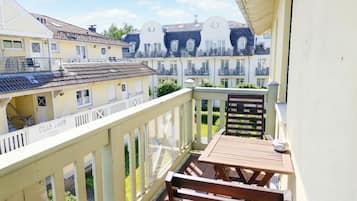 A balcony with a wooden table and bench, overlooking a row of buildings with balconies.