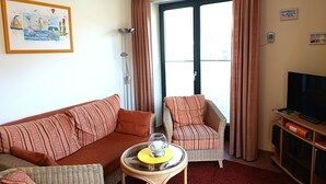 A living room with a sofa, armchair, and a TV stand with a flat-screen TV. - Villa Laura 12 - Laura 12 (Kühlungsborn)