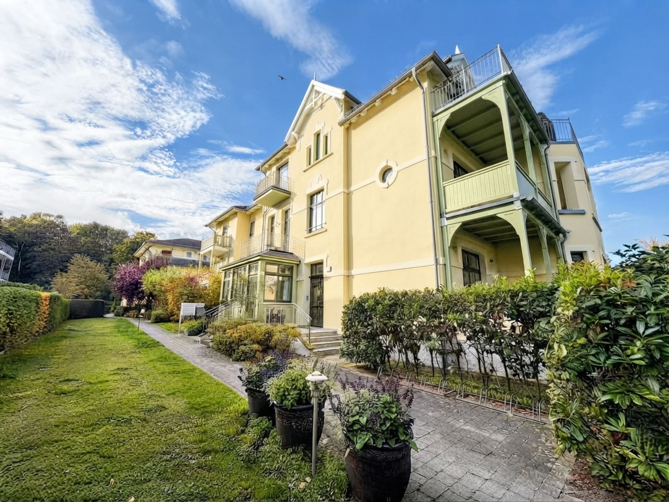 A two-story building with a balcony, a well-maintained lawn, and potted plants.