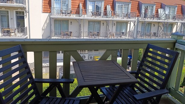 A balcony with two wooden chairs and a small table, overlooking a row of terraced houses with balconies and railings. - Villa Laura 12 - Laura 12 (Kühlungsborn)