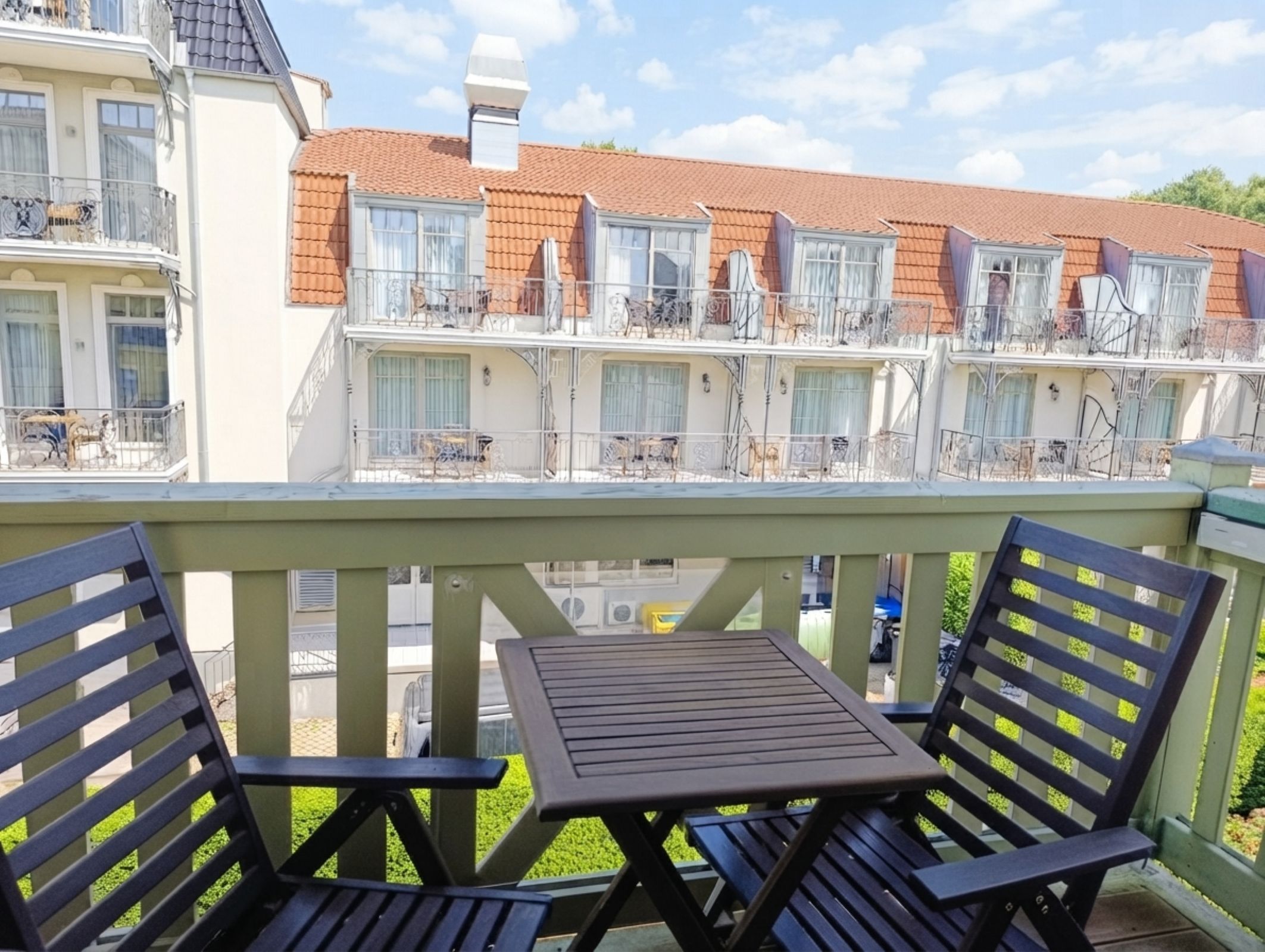 Een balkon met een tafel en stoelen, met uitzicht op een rij terraswoningen met balkons.