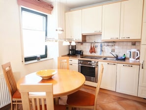 Una cocina con una mesa de madera, sillas, estufa y armarios.