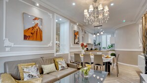 Un salon spacieux avec une table basse en verre, un canapé beige agrémenté de coussins à motifs et un lustre.