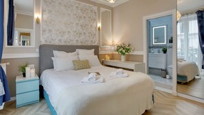 Une chambre d’hôtel avec un grand lit, des tables de chevet, une coiffeuse avec un miroir et une salle de bain visible à travers une porte ouverte.