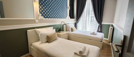 Een hotelkamer met een groot bed, een kleiner bed, een nachtkastje, een spiegel, een wandairconditioner en een raam met gordijnen.