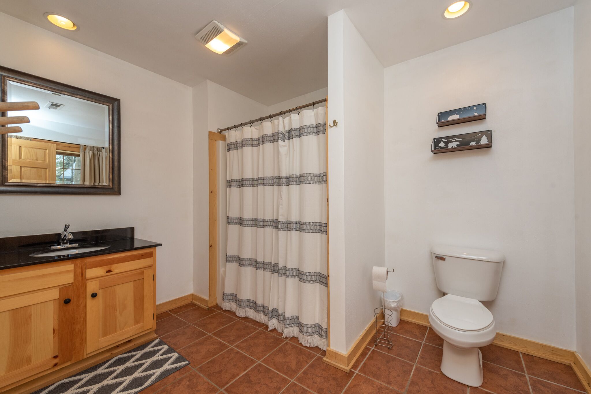Un baño con tocador de madera, inodoro blanco, cortina de ducha a rayas y espejo sobre el tocador.