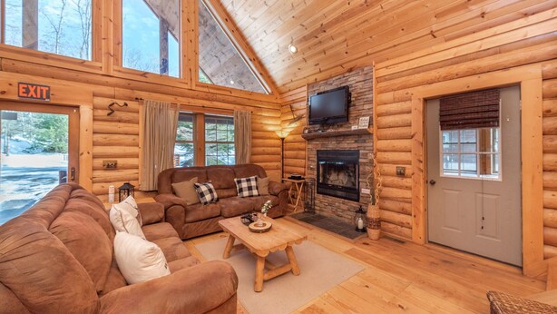L'intérieur d'une cabane en rondins, avec un grand canapé, une cheminée et un téléviseur.