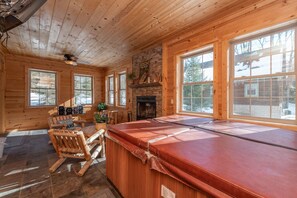 L’intérieur d’un chalet en bois, avec une cheminée, de grandes fenêtres et un jacuzzi.