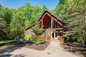 A cabin with a large porch, a covered deck, and a clear view of the surrounding forest. - Charming Log Home w/ Fireplaces & Hot Tub (Oakland)