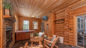 L’intérieur d’un chalet en rondins est agrémenté d’une cheminée en pierre, de fauteuils à bascule en bois, d’un bain à remous et d’un téléviseur fixé au mur.