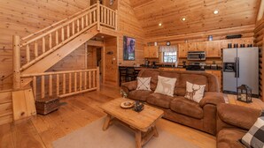L’intérieur d’une cabane en bois comprend un escalier, un salon avec un canapé et des coussins, un coin cuisine équipé d’appareils électroménagers et une table à manger.
