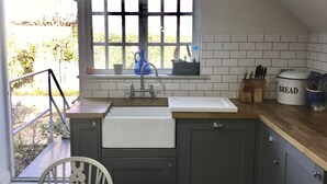 Una cocina con ventana, lavamanos y mesa de madera.