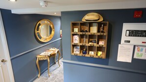 Un pasillo con pared azul, una vitrina de madera con varios objetos, un espejo redondo y una pequeña mesa con libros.