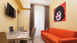 A room with a dining table, chairs, a sofa, a TV, and a painting on the wall.