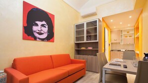 A modern living room with a bright orange sofa, a dining table with chairs, and a kitchen area visible through an open door.