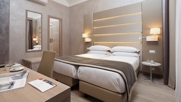 A modern hotel room with a large bed, bedside tables, a desk, and a mirror.