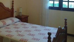 Un dormitorio con una cama de madera, una mesita de noche, una lámpara y una ventana con cortinas.