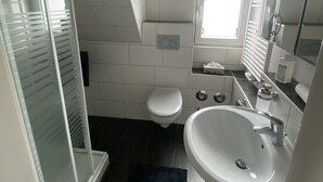 Un baño moderno con inodoro blanco, lavamanos y ducha.