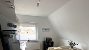 Una cocina moderna con horno empotrado, una mesa de comedor con una planta y vistas a una casa a través de una ventana.