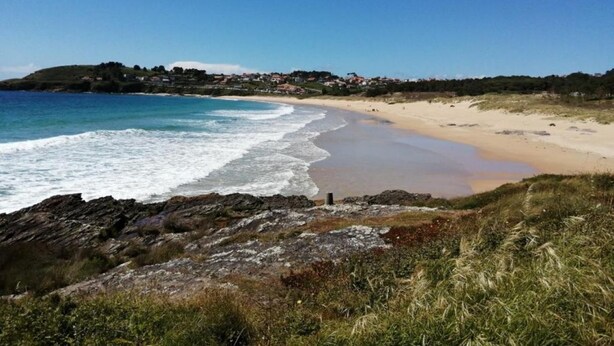 A coastal landscape with a sandy beach, rocky shoreline, and a distant village.