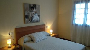A hotel room with a bed, two bedside lamps, a painting on the wall, and a window with curtains.