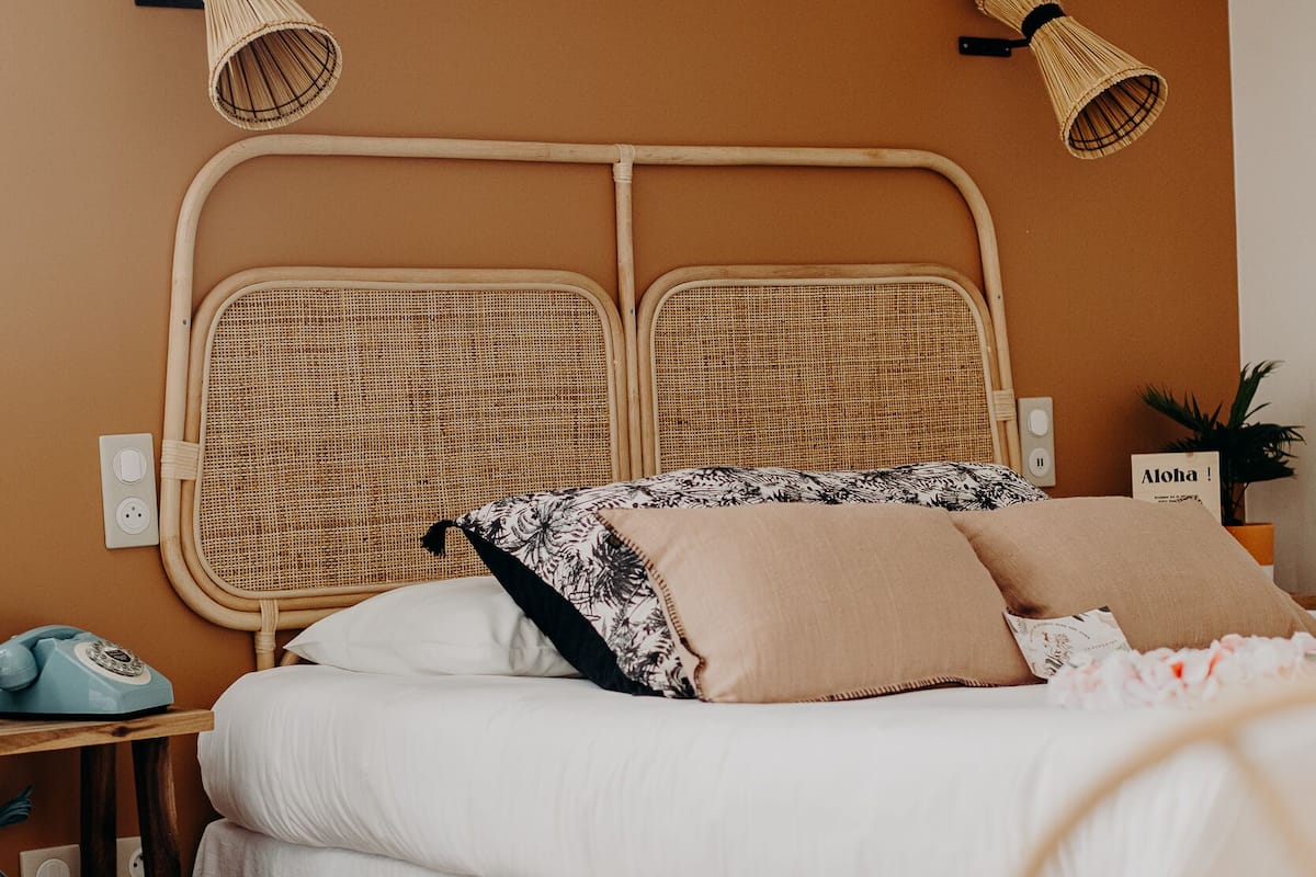 Un dormitorio con cabecera de mimbre, ropa de cama blanca y una mesita de noche con lámpara.