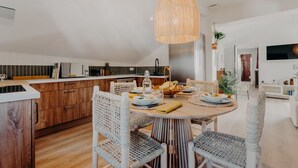 A modern kitchen with wooden cabinets, a dining area with wicker chairs, and a hanging light fixture. - Palmito (Biarritz)