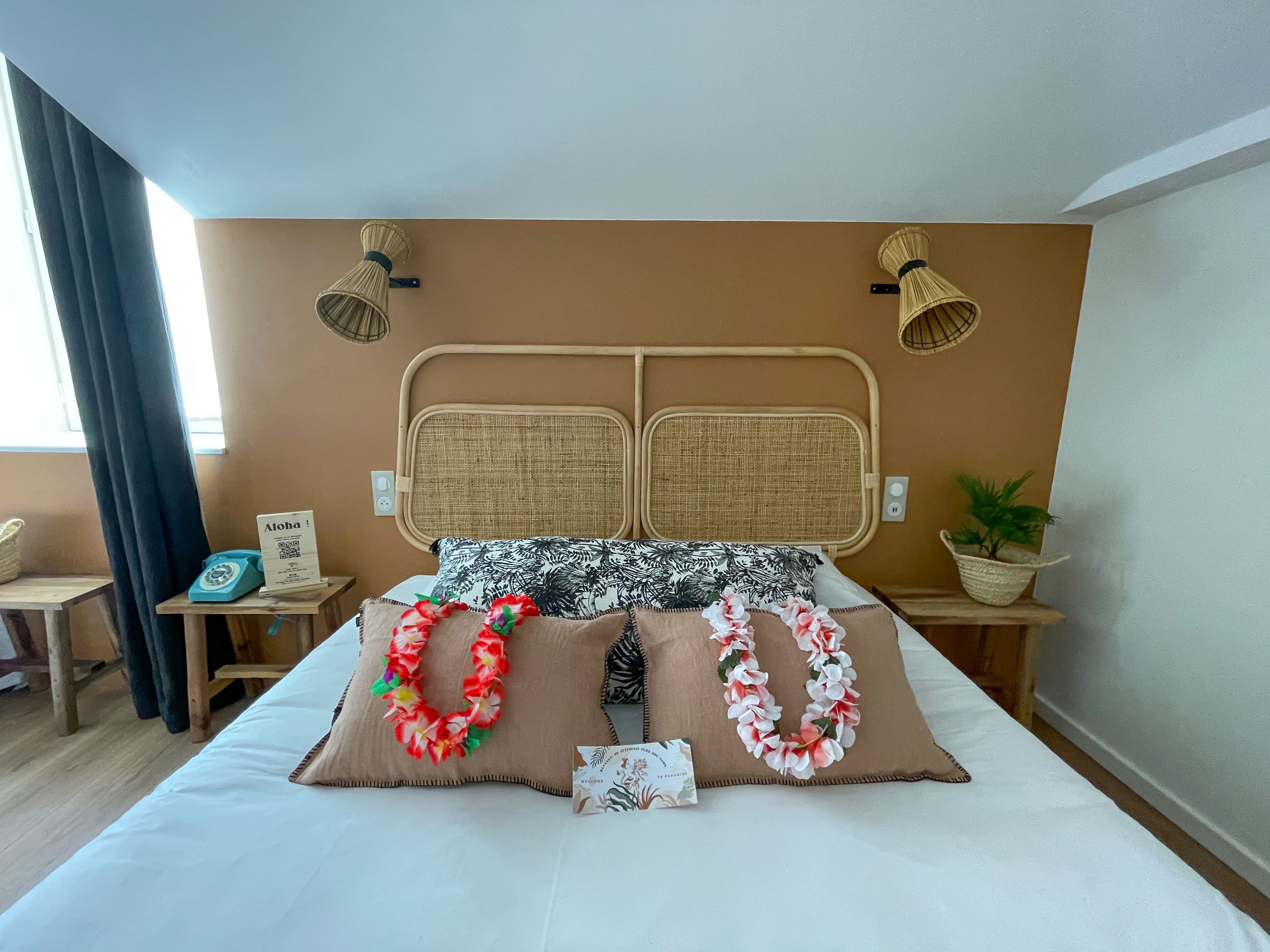 A hotel room with a bed, two nightstands, a potted plant, and a window with curtains.