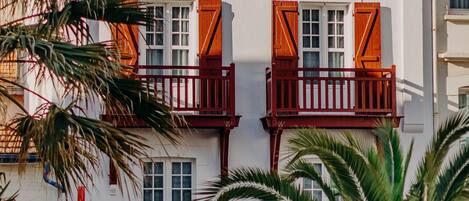 A traditional building with a white facade and red timber framing, featuring balconies with wooden shutters and a red railing.